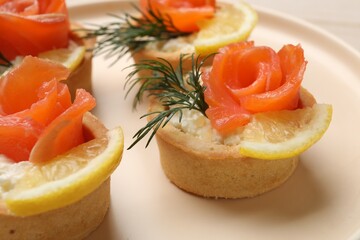 Tasty tartlets with salmon, lemon and dill on plate, closeup