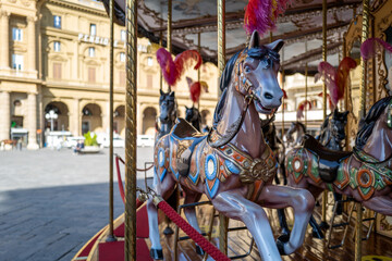 A beautifully painted carousel horse takes center stage in a charming European town square, bathed...