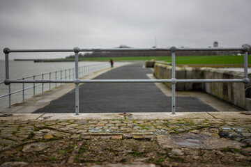 A lone walker enjoys a peaceful stroll along a seaside path, framed by a metal railing and...