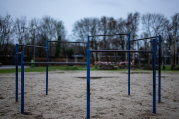 A deserted playground with blue metal bars stands on a sandy surface under a bleak sky, ready for children's play.