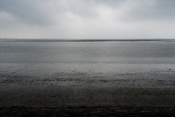 A tranquil, gray beach stretches to meet a calm, gray sea under a moody, overcast sky.