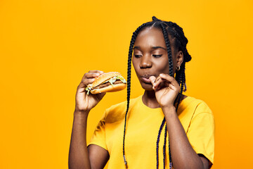 Young girl enjoying a delicious burger, wearing a bright yellow shirt, set against a vibrant yellow...