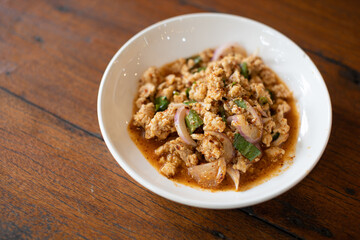 Thai Isan style pork larb served on a white plate on a wooden table.