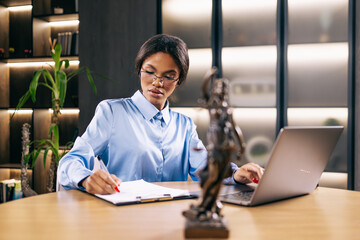 Statue of Justice with scales and a lawyer working on a laptop. Concept: legal consultations and...