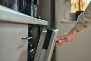 Close-up of female hand opening door of built-in dishwasher in modern kitchen. Energy-efficient...