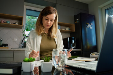 Woman sitting at kitchen table overwhelmed with bills and receipts. Financial stress and personal...