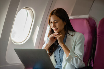 an asian woman is traveling abroad for vacation by plane, female traveler using her electronic device in an airplane to entertain herself, young woman flying abroad, journey, passenger, flight