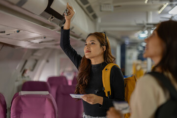 two beautiful female friends are traveling abroad on a vacation by plane, they walk to find their seats and store their bags in the overhead compartment, passenger, airplane, vacations