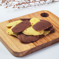 Indonesian lidah kucing. A variety of cookies in different colors are presented on a wooden board, surrounded by subtle decorative branches, creating an inviting display