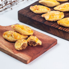 Indonesian nastar snack with pineapple jam filling. Golden pastries rest on a wooden platter, with one cut open to reveal a sweet filling, perfect for a snack or dessert