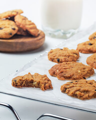 Freshly baked chocolate chip cookies are arranged on parchment paper next to a glass of milk, creating a delightful treat display