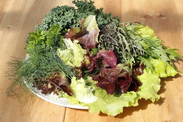 Fresh mixed salad greens on wooden table in natural light