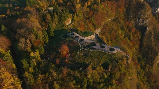 Aerial shot showcasing the historical Fort of Punta Corbin surrounded by colorful autumnal forest enveloping dramatic terrain. A serene and picturesque scene featuring rich seasonal tones.