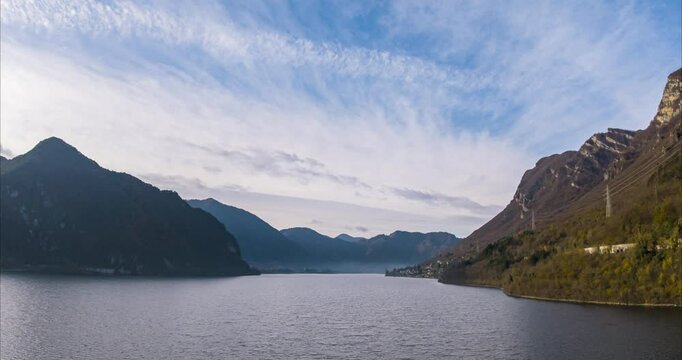 Aerial timelapse view of Lake Idro, an Italian pre alpine lake of glacial origin, reflecting morning light under a blue sky with clouds.rising shot
