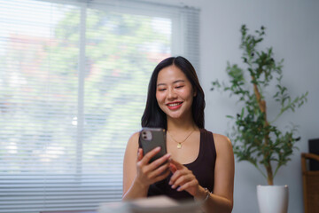 Young Asian Woman Using Smartphone at Home Smiling