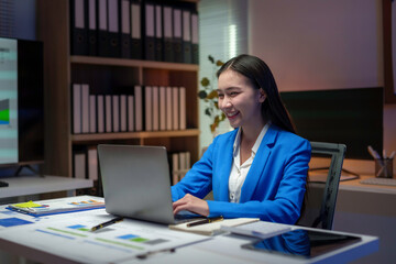 Asian businesswoman working with laptop and smiling in office at night