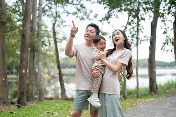 Fototapeta premium A happy Asian mom and dad carrying their little boy together while walking in a public park.