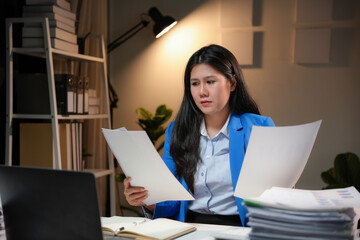 Asian businesswoman working late comparing documents at her desk