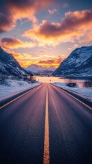 Fototapeta premium Scenic Road Through Snowy Mountains at Sunset with Vibrant Sky and Golden Reflecting Light