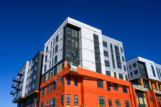 New multistory mixed use commercial and residential building under construction on a sunny winter day, orange building wrap, exterior walls and windows
