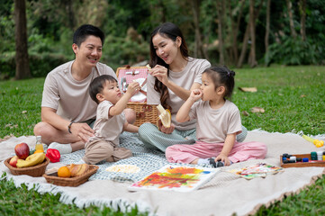 A cheerful Asian family enjoys a picnic, eating, and playing with their little boy and girl.