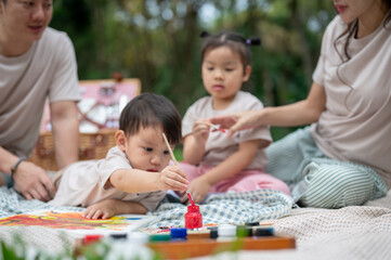 Obraz premium A cute little Asian boy enjoys painting on a canvas while picnicking with his parents and sister.