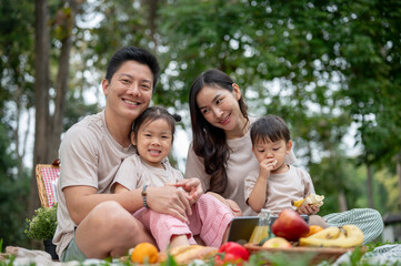 Caring Asian parents enjoy a picnic in a public park with their little kids.