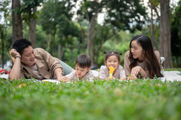 A happy Asian family lying on a picnic blanket in a park, enjoying a fun picnic time together.