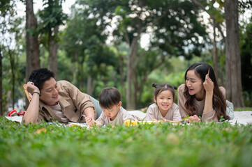 A happy Asian family lying on a picnic blanket in a park, enjoying a fun picnic time together.