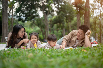 Fototapeta premium A happy Asian family lying on a picnic blanket in a park, enjoying a fun picnic time together.
