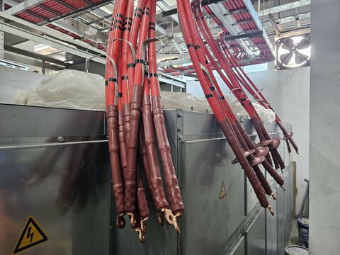 Medium voltage cables red colored with copper connectors hanging over an electrical panel in an industrial setting, highlighting infrastructure power distribution in progress