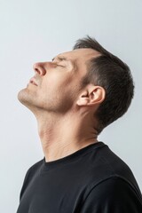 Fototapeta premium Profile of a man with eyes closed, head tilted back, serene expression, black shirt, studio shot, simple background