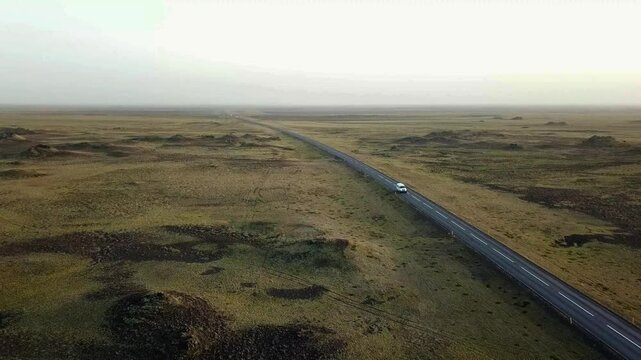 A solitary car travels along a long, open road cutting through the vast, rugged volcanic terrain of G&ouml;ngulei&eth; um Eldhraun, offering a serene view of Iceland's striking and untouched natural beauty