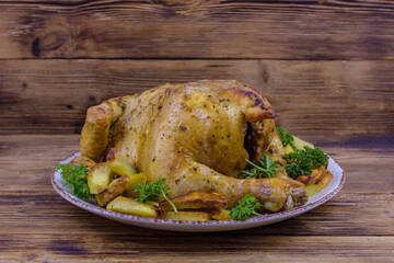 Plate with baked chicken and potatoes on a wooden background