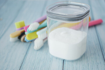 A wooden bowl of baking soda, a bamboo toothbrush, and a glass jar on a fabric