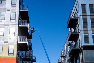 New multistory mixed use commercial and residential building under construction on a sunny winter day, construction worker in a lift bucket working up high, sun reflecting window glass and building si