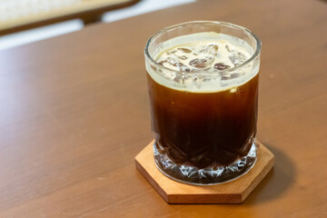 Close-up of an iced black Americano coffee in a transparent glass cup with crystal-clear ice cubes, placed on a wooden coaster on a wooden table