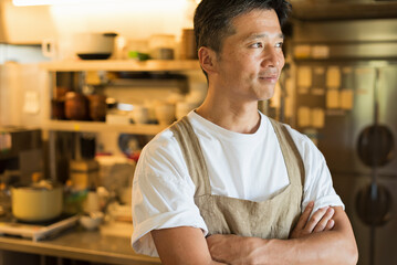 カフェのキッチンを背景に立つ40代男性シェフ