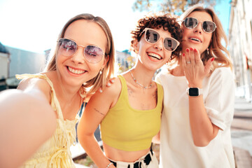 Three young beautiful smiling hipster female in trendy summer stylish clothes. Sexy carefree women posing in the street. Positive models having fun, hugging and going crazy, in sunny day, take selfie