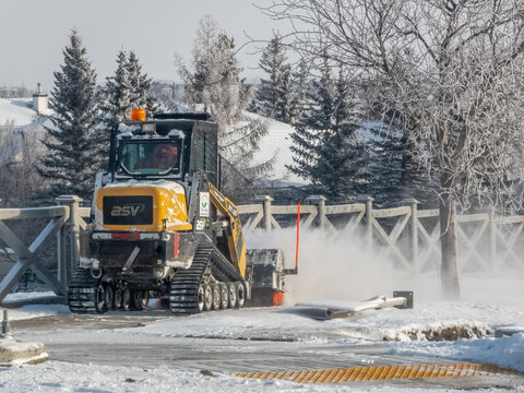 Calgary, Alberta, Canada. Feb 2, 2025. A yellow ASV RT-30 compact track loader clears snow from a path, its powerful tracks and efficient design tackling winter's challenges. Snowflakes fill the air.