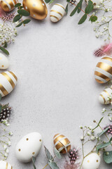 Easter eggs frame decorating a gray surface with eucalyptus leaves and feathers