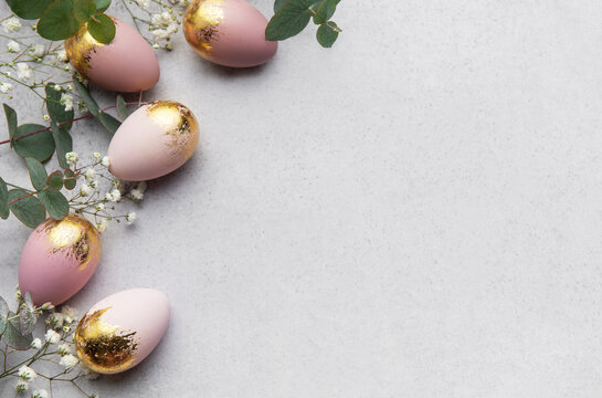 Elegant easter eggs with gold leaf and eucalyptus leaves creating a border on gray background