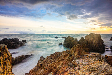 Serene sunset seascape, ocean waves softly caress rocky shoreline under a vibrant sky.  
  