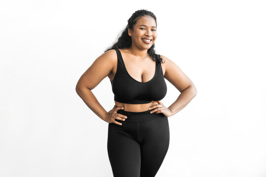 Losing weight concept. Studio image of young attractive african american plus size woman in black leggings and crop top posing against white copy space background, challenging herself