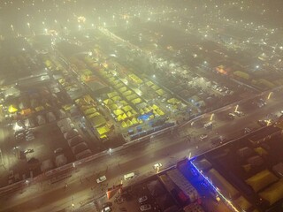 Drone view of Mahakumbh tent city at night, wrapped in fog with glowing tents. A mystical and...