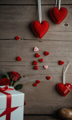 Valentine's Day themed composition with red hearts, scattered petals, and a gift box on a rustic wooden background.