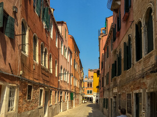 Fototapeta premium A Narrow Venetian Alleyway. A narrow alleyway winds its way through the city, lined with colorful buildings that lean in towards each other. 