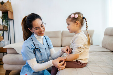Smiling doctor putting adhesive bandage on little girl's wound at her home visit.