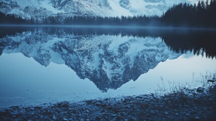 A symmetrical reflection of rugged snow-covered peaks in a still, cold lake creates a breathtaking vista of tranquility and natural splendor.