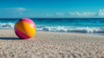 Obraz premium Bright beach ball resting on sandy shore with ocean waves and clouds in the background